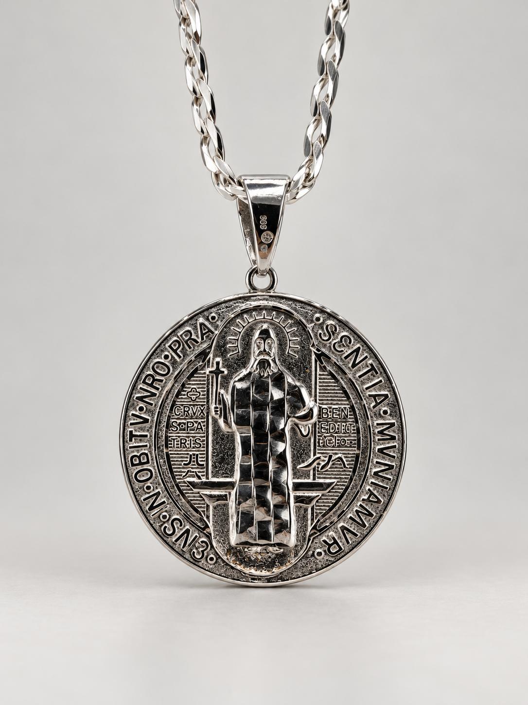 Silver-tone round Saint Benedict pendant with surrounding inscriptions and dark recessed details