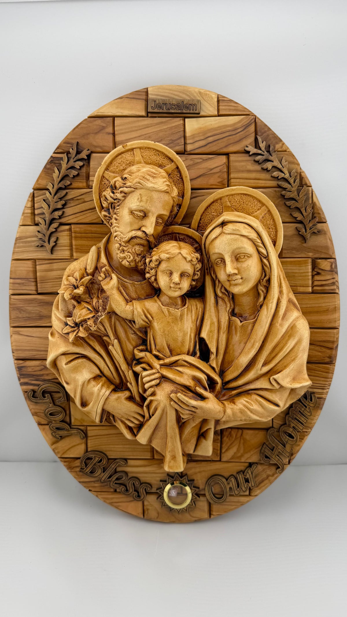 Oval olive wood Holy Family wall plaque with Joseph, Mary, and Jesus, Jerusalem at the top, and God Bless Our Home lettering below